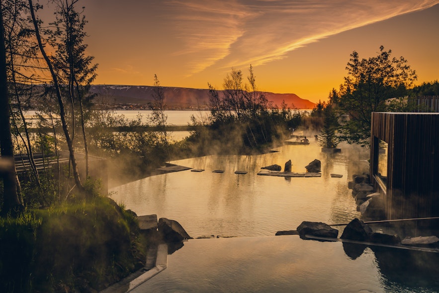 Steam rises from Iceland's Forest Lagoon under the midnight sun.