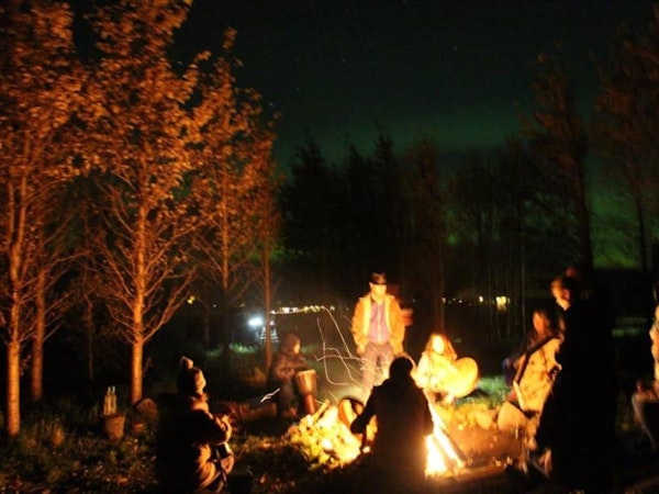 Friends sit around a campfire when staying at Esjan, a glamping experience in converted buses near Reykjavik.