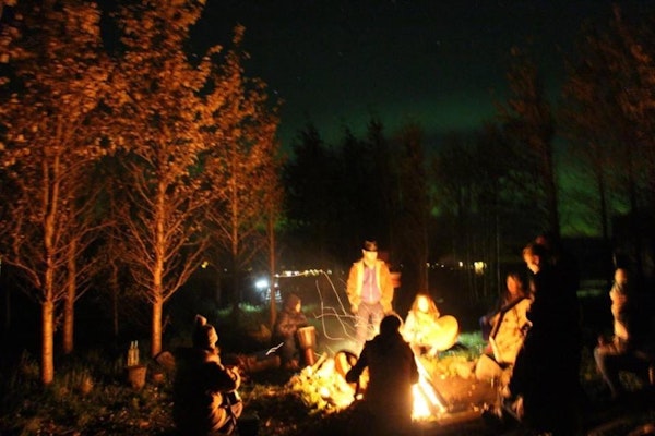 Friends sit around a campfire when staying at Esjan, a glamping experience in converted buses near Reykjavik.