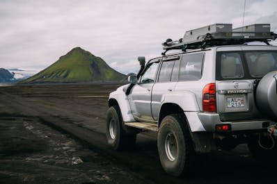 A 4x4 vehicle traverses a black sand desert in the Icelandic Highlands.