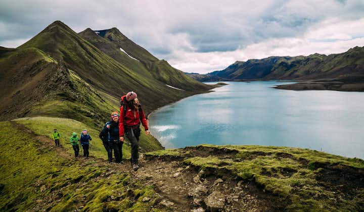 Hikers look out over a blue glacial lake nestled in the Highlands of Iceland.