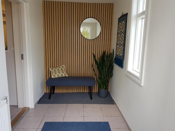A hallway with homey touches, such as a comfortable seat, mirror, plant, and wall tapestry at Guesthouse Mikael.