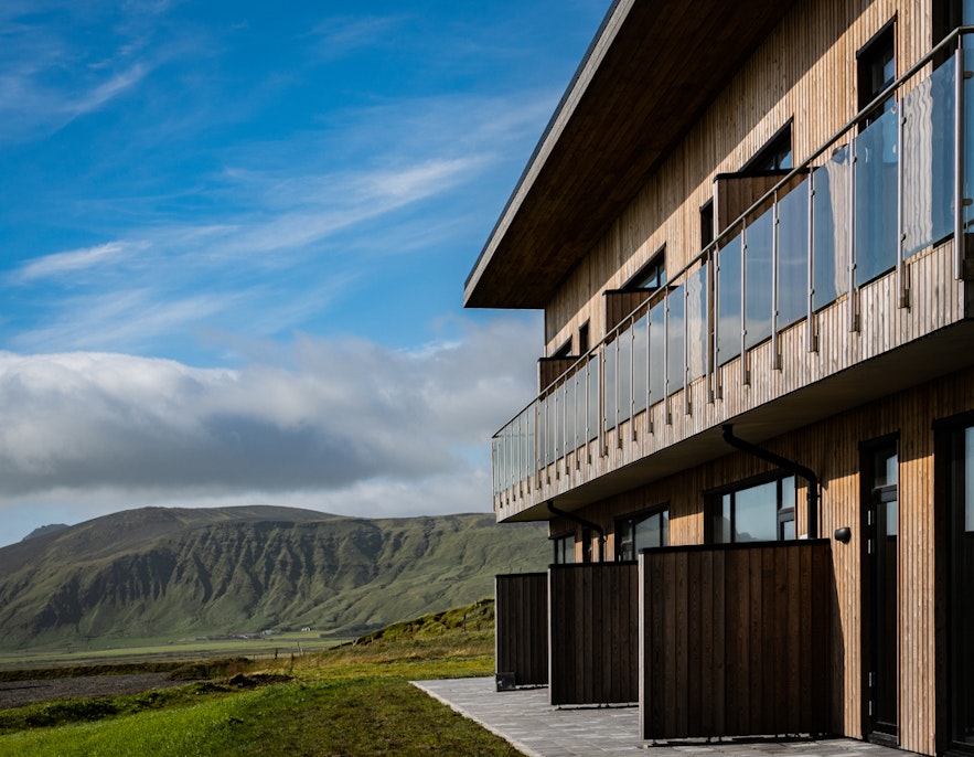 An external view of the Black Beach Suites accommodation in South Iceland, with green mountains in the distance.