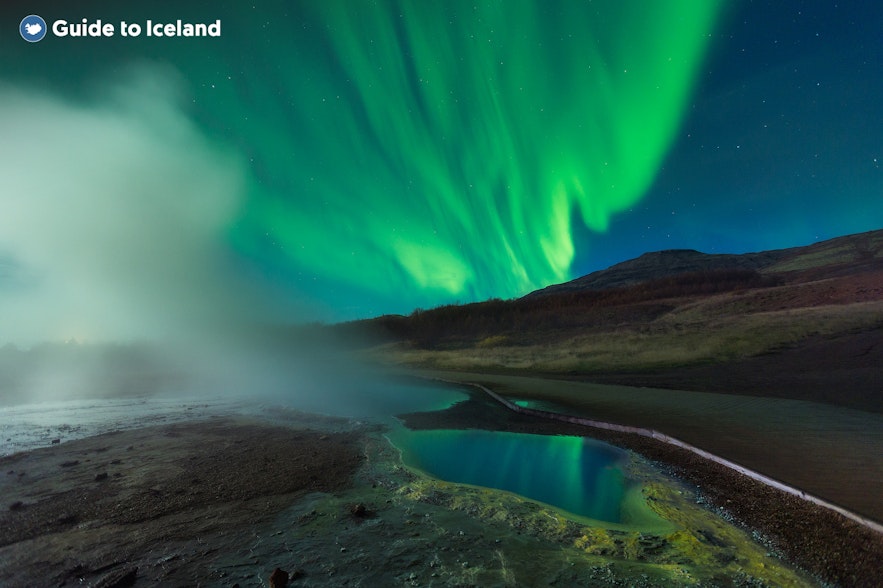 The northern lights appear over the hot springs at Geysir.