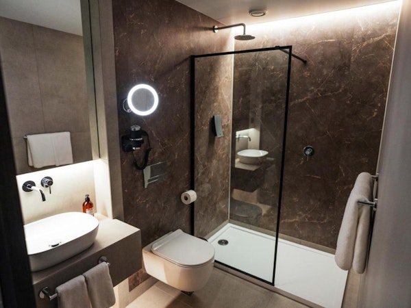 A modern bathroom with a toilet, shower, basin, and towels at Konvin Hotel by Keflavik Airport.