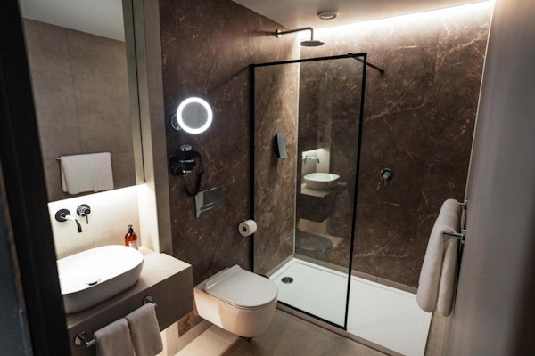A modern bathroom with a toilet, shower, basin, and towels at Konvin Hotel by Keflavik Airport.