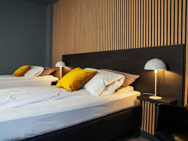 A double bed with cushions and a bedside lamp at Konvin Hotel by Keflavik Airport.