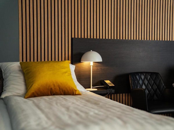 A close-up view of a bed and lamp at Konvin Hotel by Keflavik Airport.