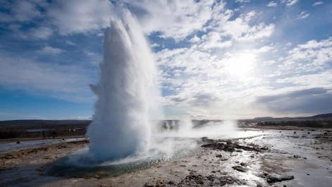 The Strokkur geyser erupts with boiling water and steam, showcasing the raw power of Iceland's volcanic activity.