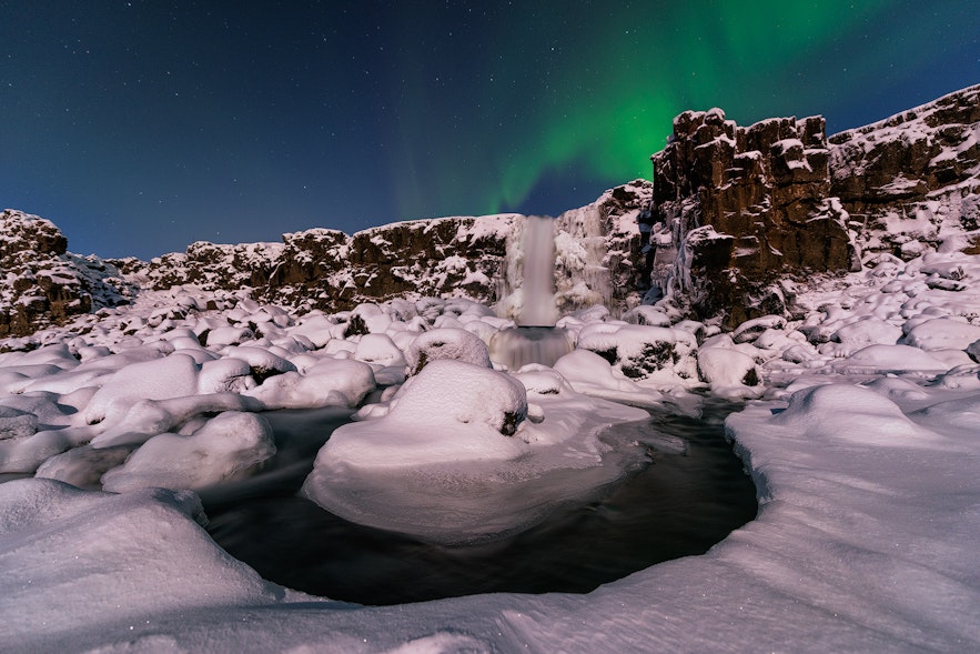 Zorza polarna na niebie nad wodospadem Oxararfoss w Parku Narodowym Thingvellir na Islandii zimą.