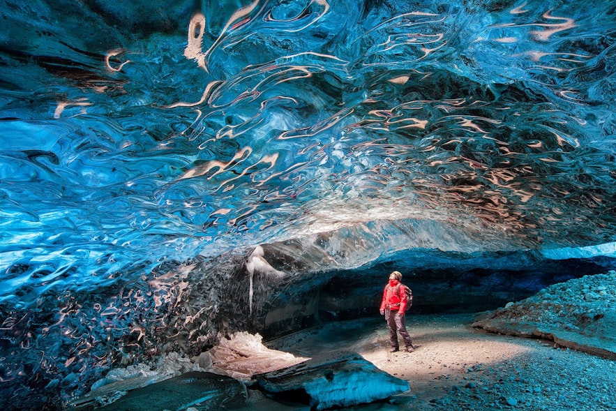 Osoba zwiedzająca jaskinię lodowcową na Islandii zimą, wyposażona w odpowiednią odzież i sprzęt.