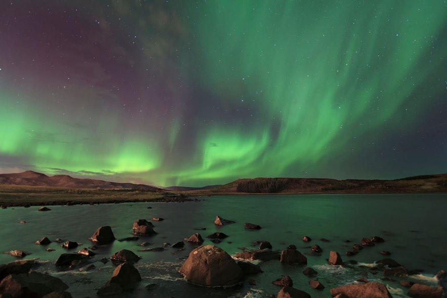 แสงเหนือบนฟ้าที่มีดาวพร่างพรายเหนือทะเลสาบในฤดูใบไม้ร่วงในไอซ์แลนด์