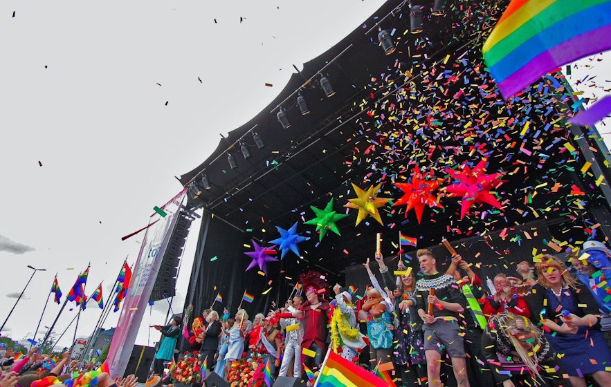 Koniec koncertu podczas Gay Pride w Reykjaviku, pokazujący tęczowe flagi, konfetti i ludzi przebranych w kostiumy.