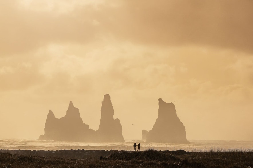 霧に包まれたアイスランドの黒砂海岸を散策する観光客。南海岸のヴィーク村にて