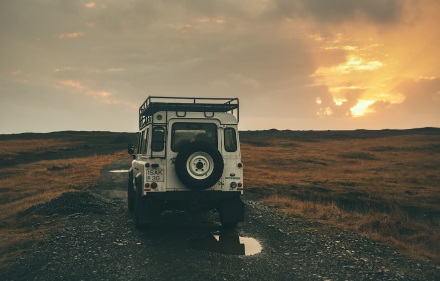 รถจี๊ปขับรถบนถนนลูกรังที่มีหลุมและน้ำฝนในยามพระอาทิตย์ตกในไอซ์แลนด์ในฤดูใบไม้ร่วง