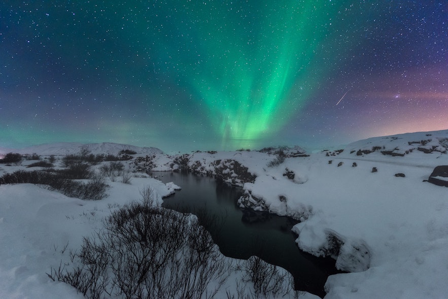 Thingvellir in winter covered in snow in a starry night with the green northern lights in the sky and a shooting star