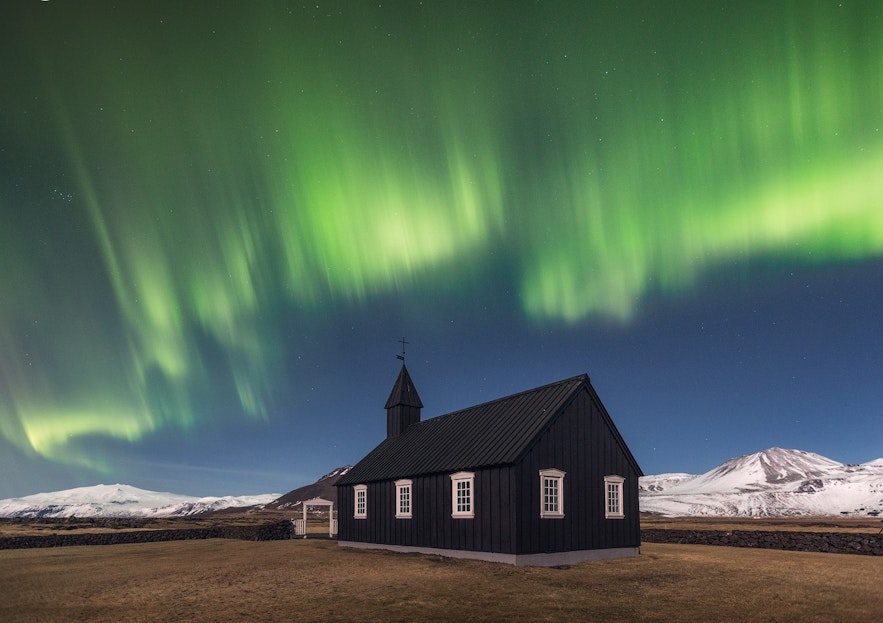 Budir church on the Snaefellsnes peninsula with snowy mountains in the background and northern lights in the night sky