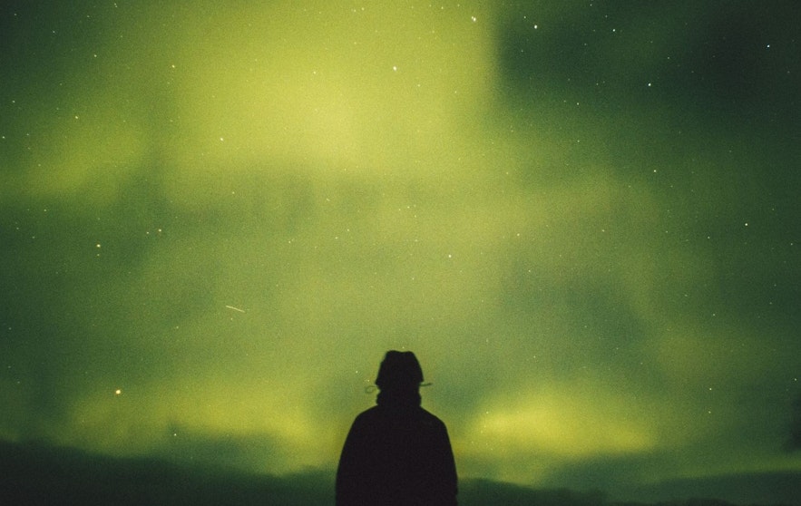 Person standing outside in the night observing the green northern lights