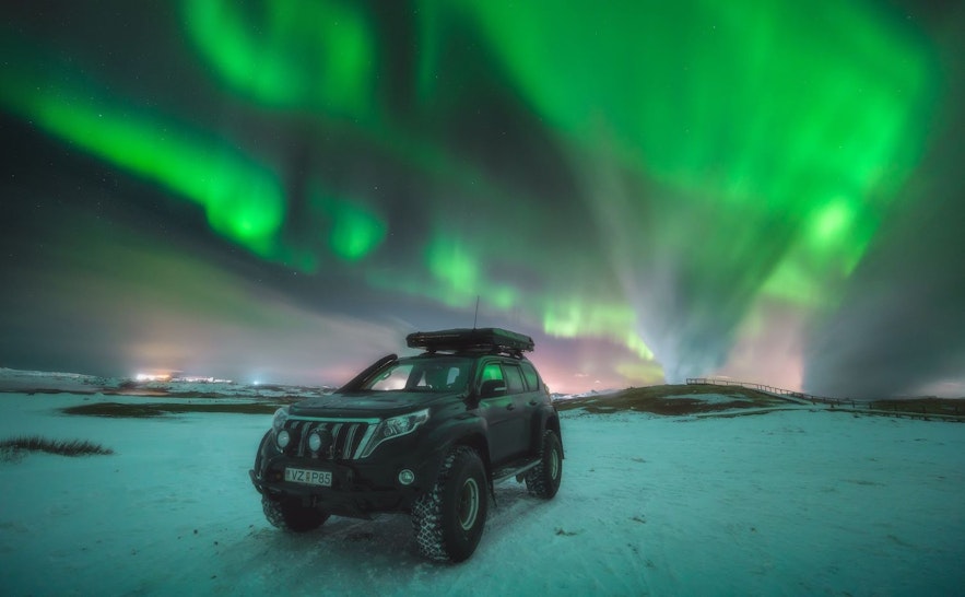 Large jeep from a northern lights jeep tour, parked in the snow by Gunnuhver on the Reykjanes Peninsula with the aurora borealis in the sky